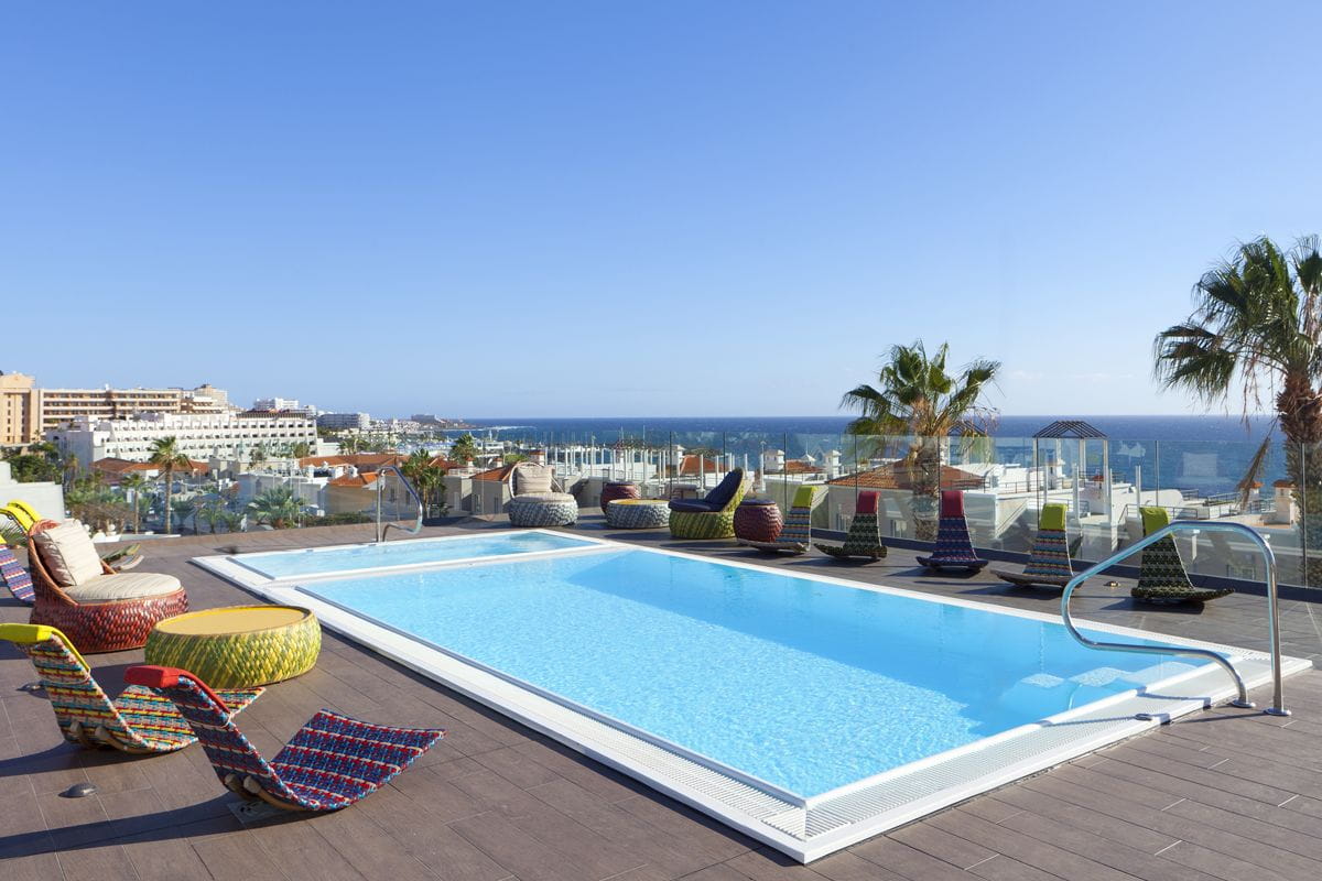 Piscina en azotea con vistas al mar en Tenerife. Palmera y edificios al fondo.