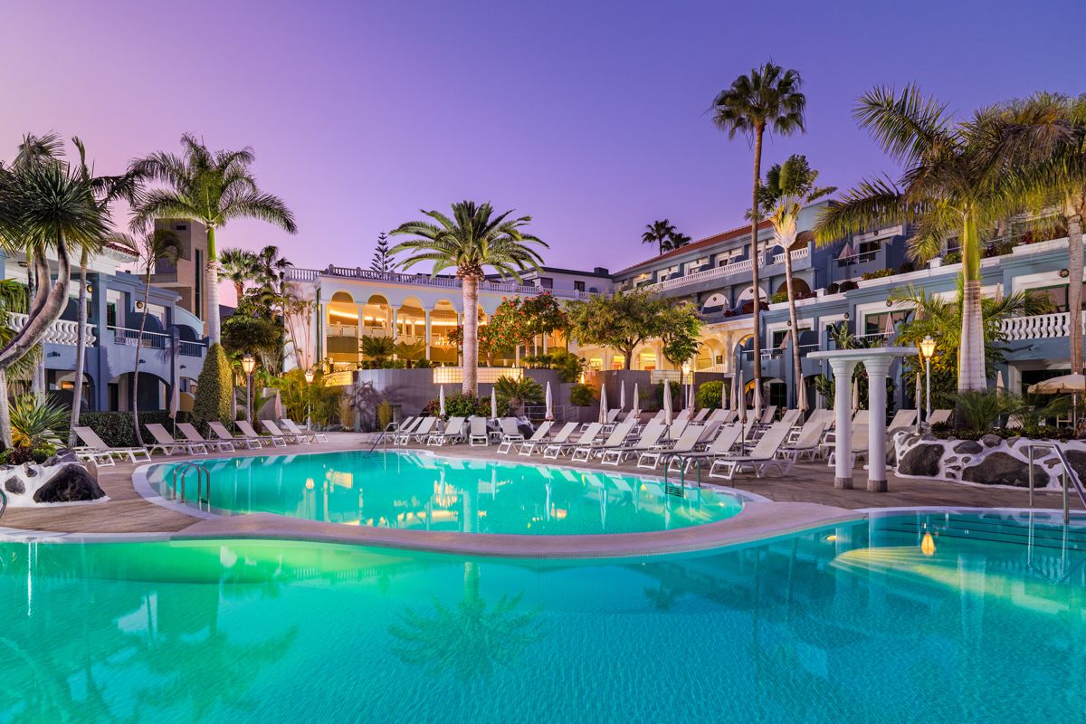Piscina del hotel rodeada de palmeras al atardecer en Tenerife.