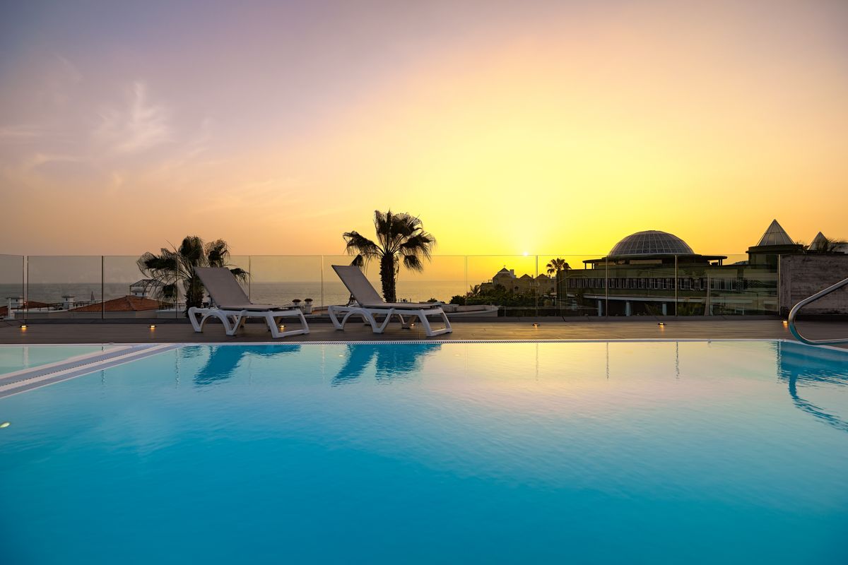Piscina al atardecer en Tenerife con tumbonas y palmeras.