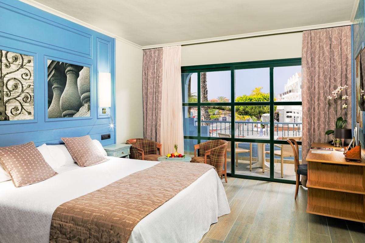 Habitación de hotel con cama doble, muebles y balcón con vista en Tenerife.