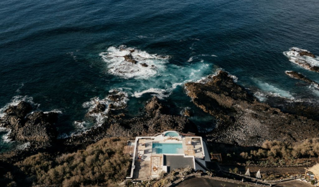 Piscina y océano en la costa de Tenerife, rodeados de rocas y vegetación.