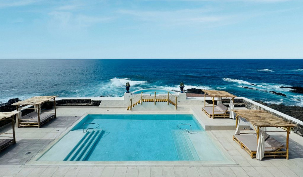 Piscina con vista al mar en Tenerife, rodeada de camas con toldo.