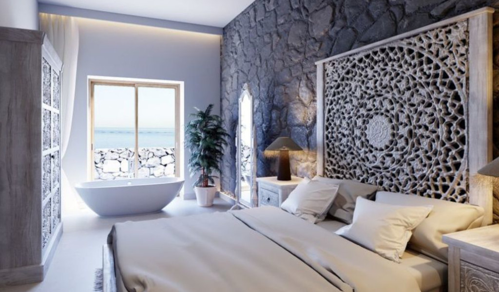 Dormitorio con ventana al mar en Tenerife, baño freestanding y cabecero tallado.