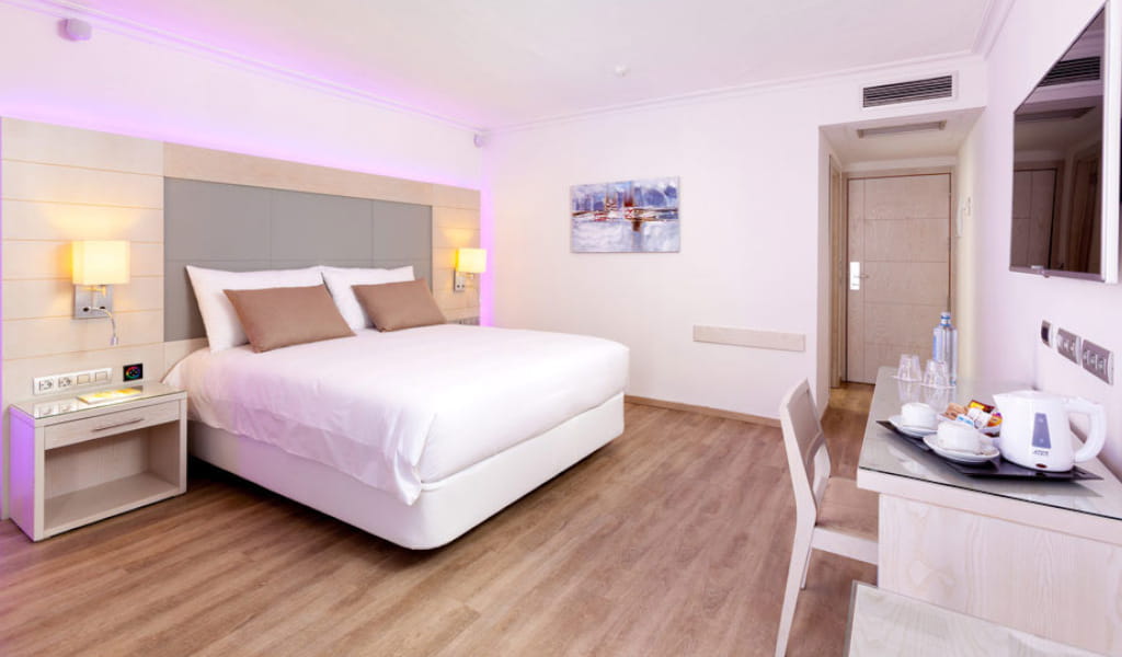 Habitación moderna de hotel en Tenerife con cama doble, escritorio y cuadro en la pared.