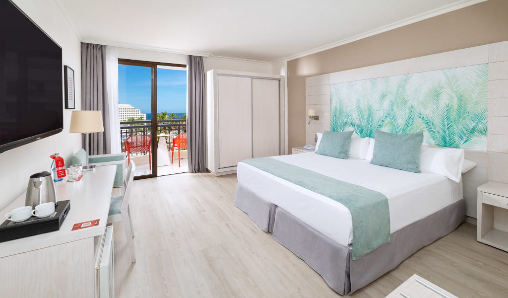 Habitación de hotel en Tenerife con cama doble, escritorio y balcón con vista al mar.
