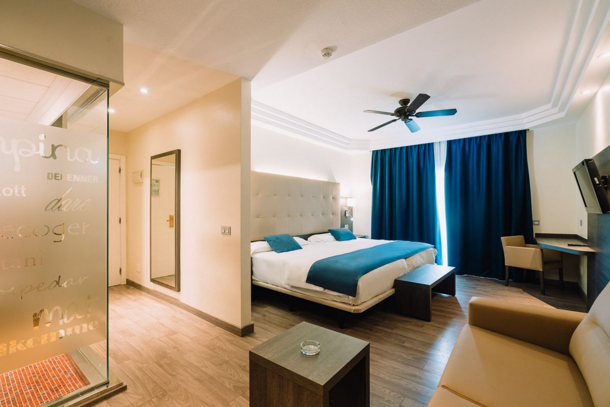 Habitación de hotel en Tenerife con cama doble, sofá y cortinas azules.