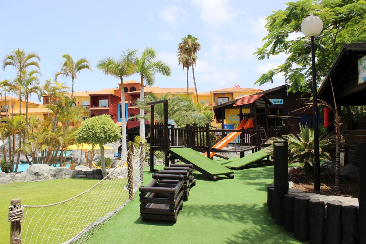 Área de juegos con tobogán y palmeras en resort de Tenerife.