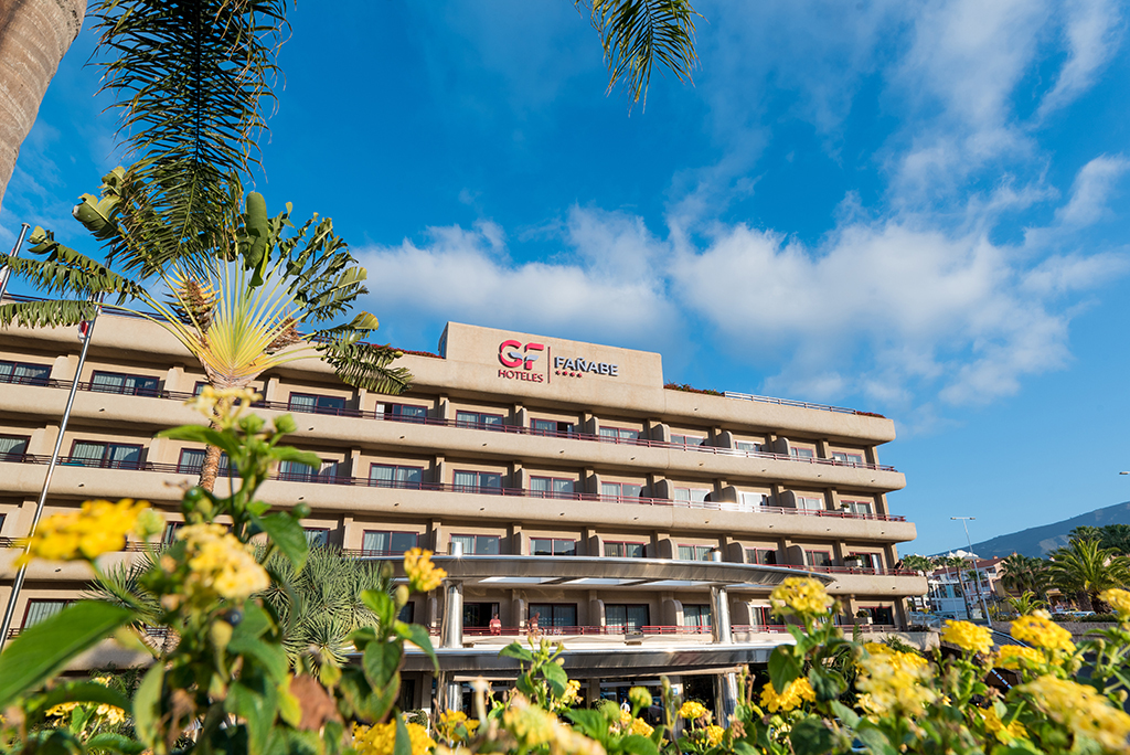 Hotel GF Fañabé en Tenerife con flores y palmeras en primer plano.