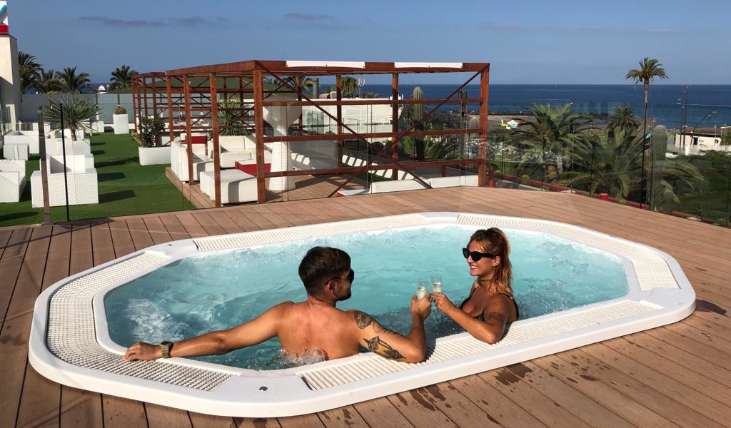 Personas en jacuzzi brindando con vista al mar en hotel de Tenerife.