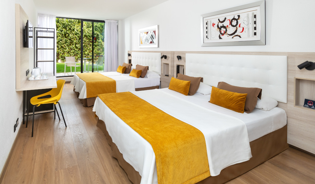 Habitación de hotel en Tenerife con dos camas dobles, escritorio y vista al jardín.