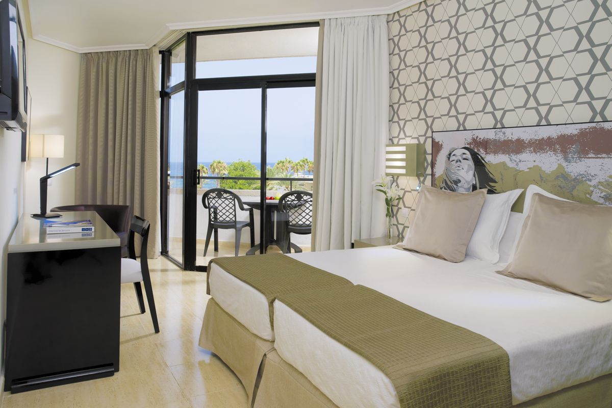 Habitación de hotel en Tenerife con cama, escritorio y balcón vista al mar.