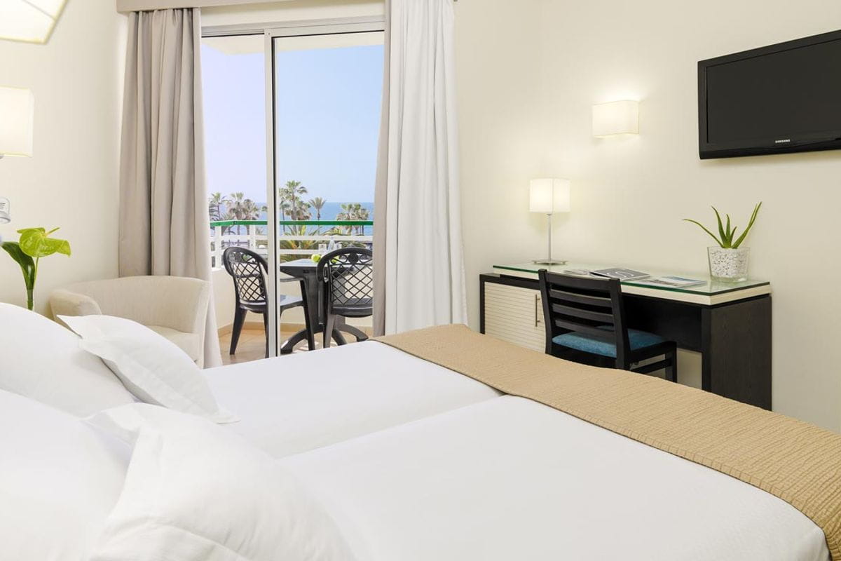 Habitación de hotel en Tenerife con cama, escritorio, balcón y vista al mar.