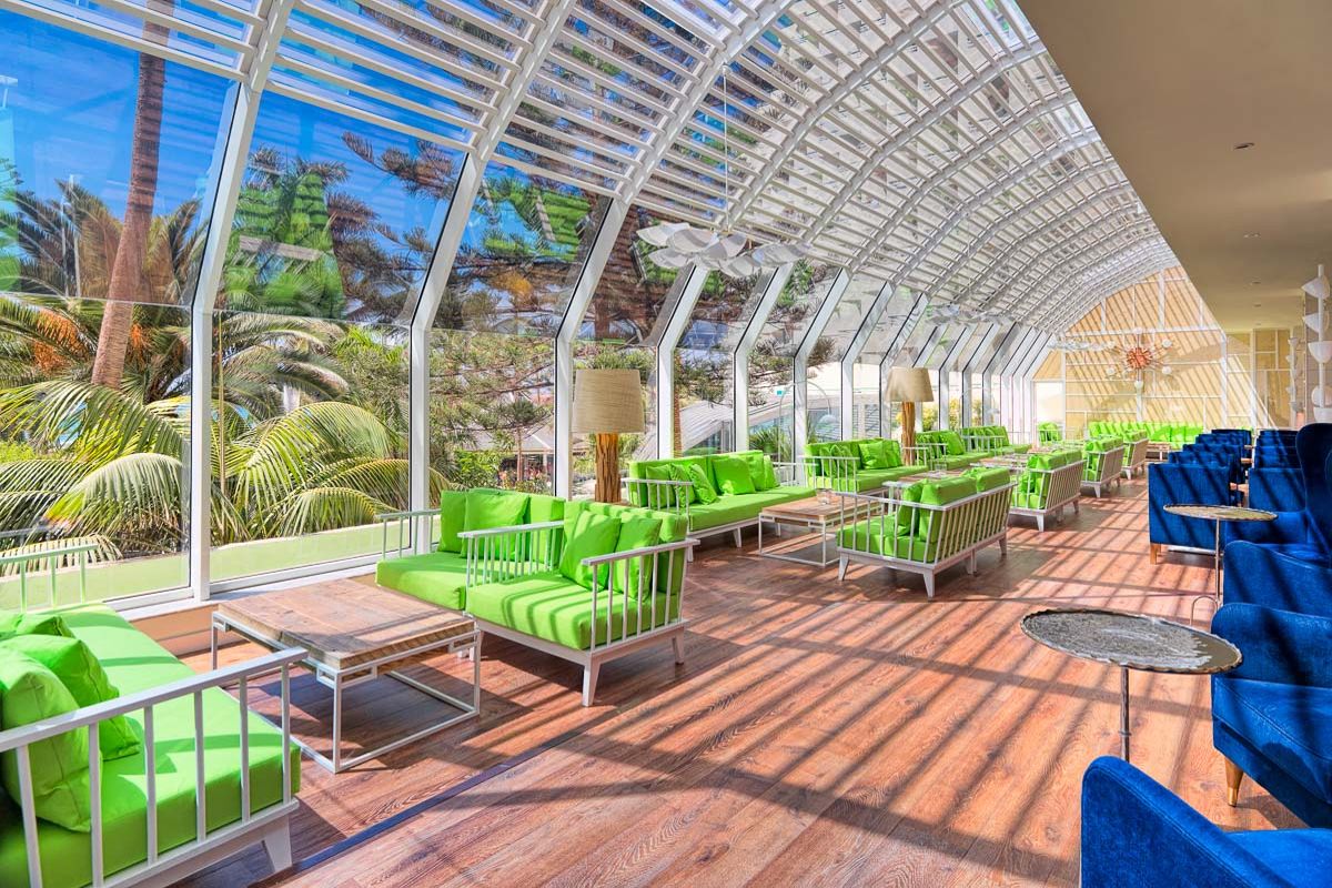 Sala iluminada con sofás verdes y azules en Tenerife con palmeras afuera.