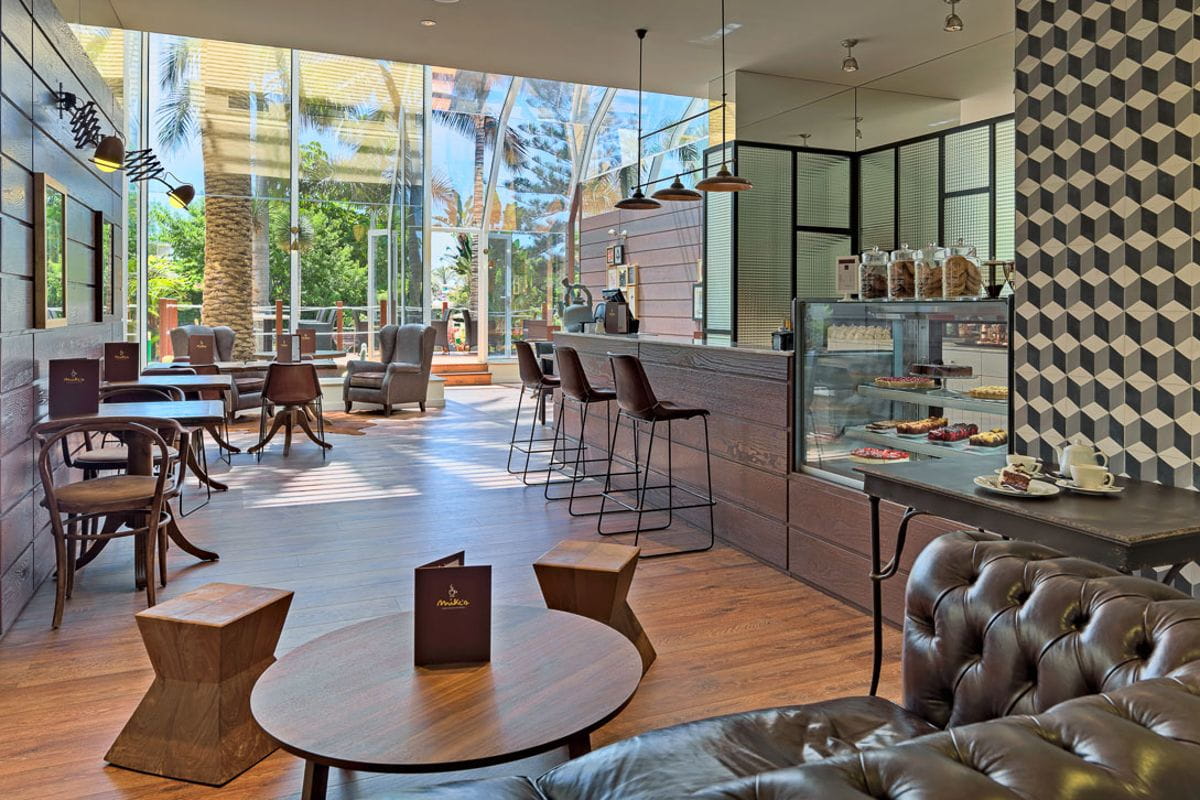 Cafetería moderna en Tenerife con muebles de madera, vitrinas de pasteles y ventanales grandes.