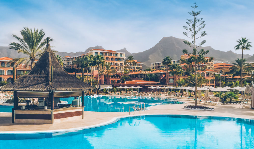 Piscina del hotel en Tenerife con montañas al fondo y sombrillas.