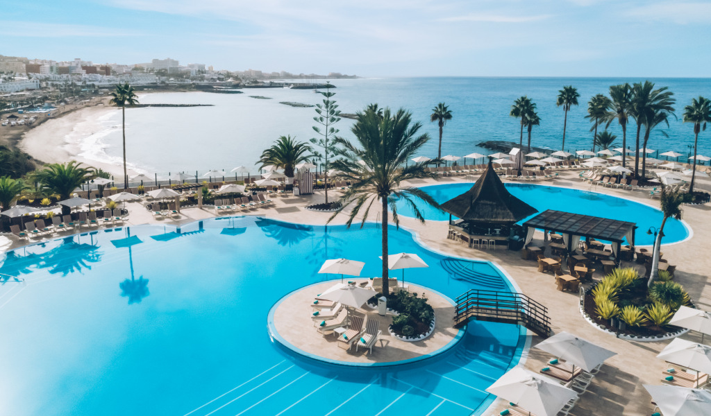 Piscina del hotel con vista al mar en Tenerife y palmeras alrededor.