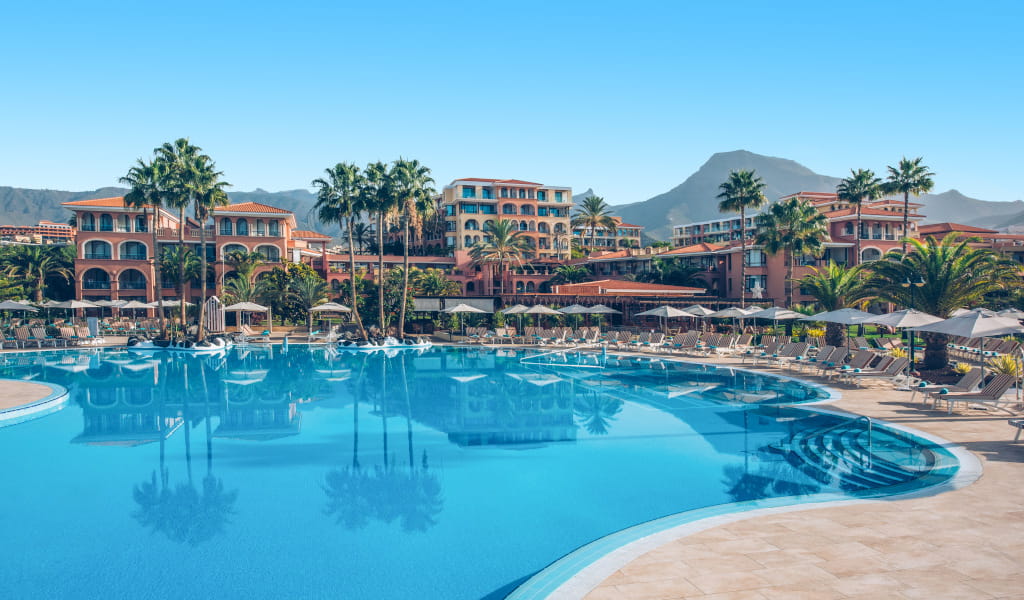 Piscina de un hotel rodeada de palmeras y montañas en Tenerife.