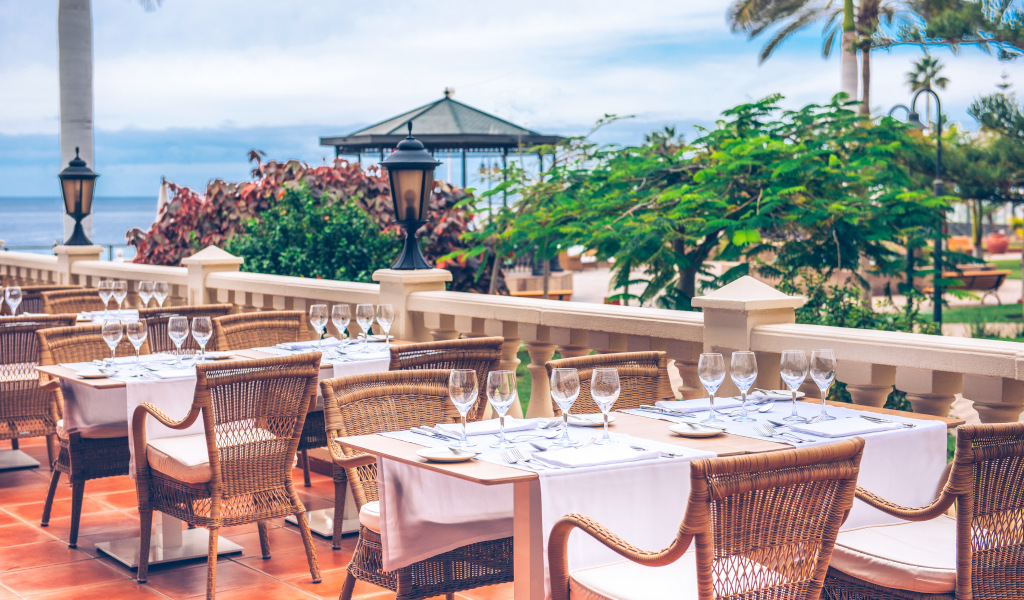 Terraza con mesas y sillas en un restaurante en Tenerife, vista al mar de fondo.