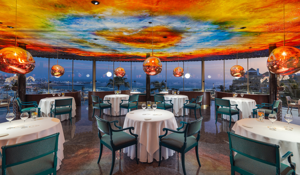 Restaurante con vista al mar al anochecer en Tenerife, lámparas colgantes y techo colorido.
