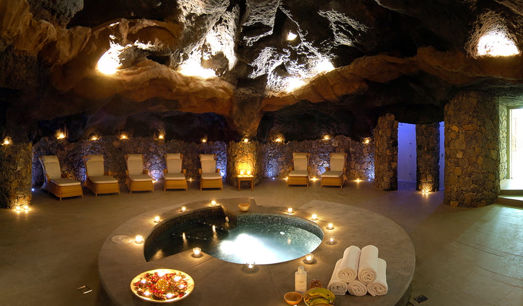 Piscina de spa en cueva iluminada con velas y tumbonas en Tenerife.