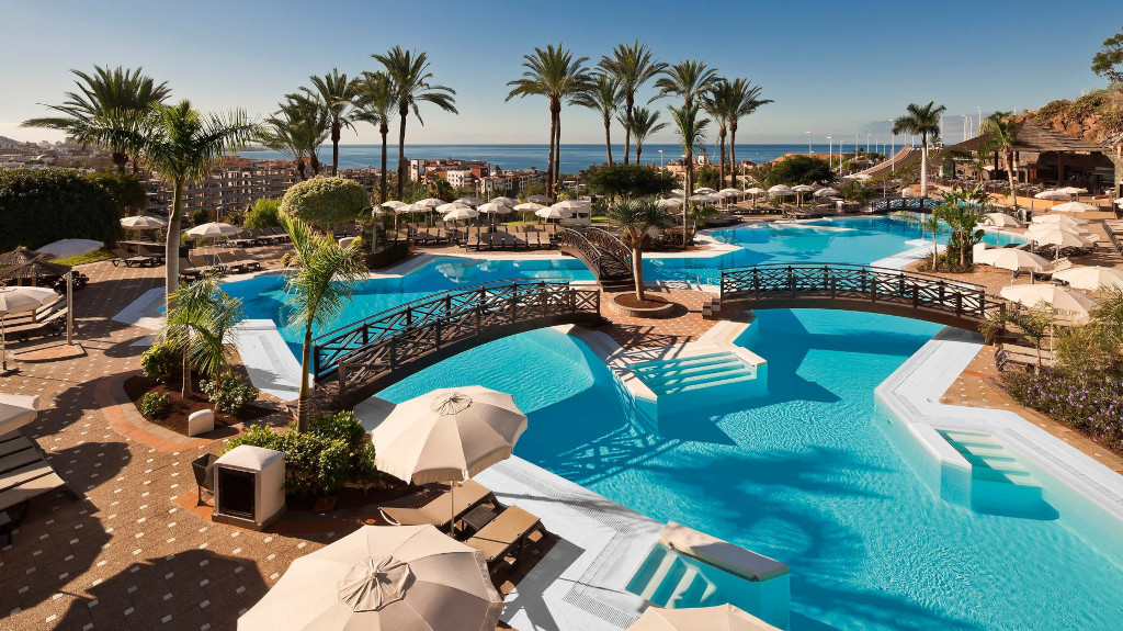 Piscina al aire libre rodeada de palmeras y tumbonas en un hotel de Tenerife.