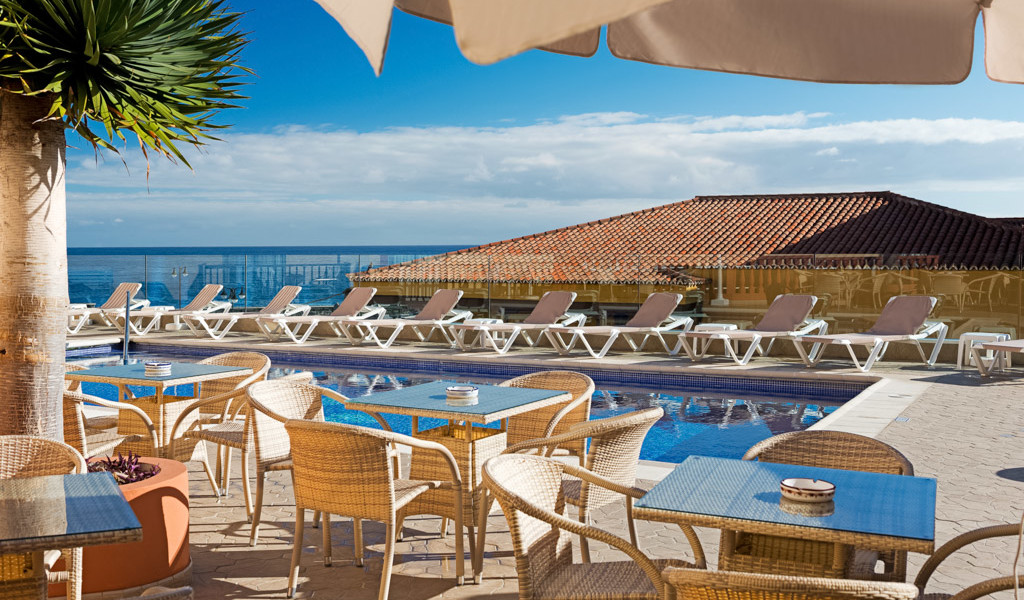 Terraza con mesas y sillas junto a piscina y tumbonas, vista al mar en Tenerife.