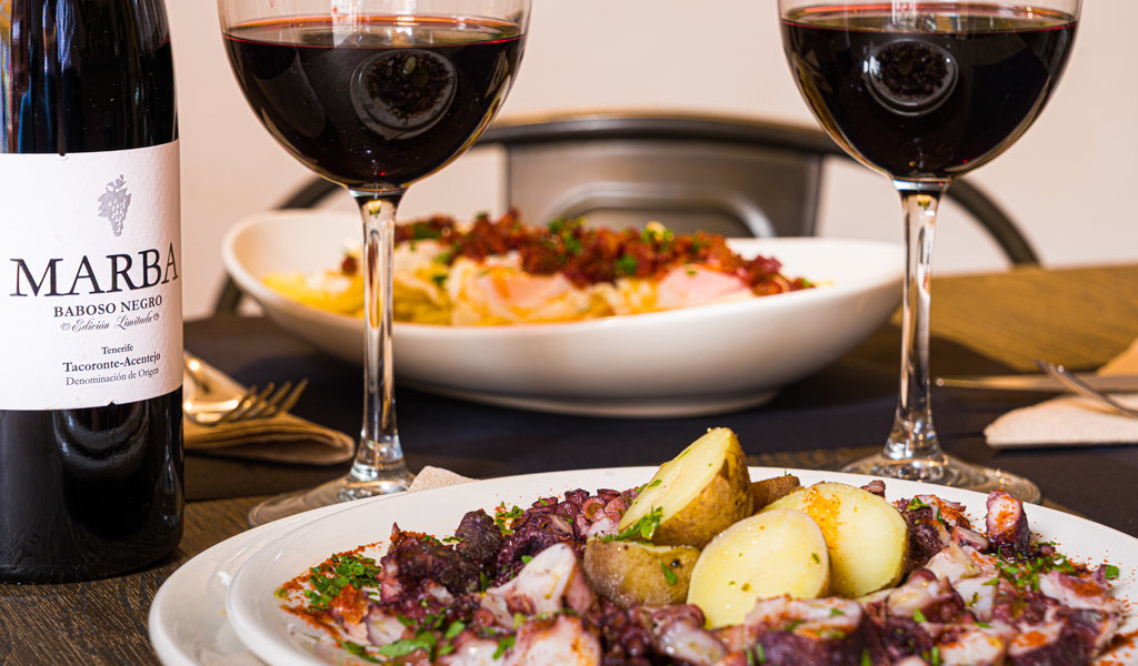 Plato de pulpo con papas, botella de Marba Baboso Negro y dos copas de vino tinto en Tacoronte-Acentejo.