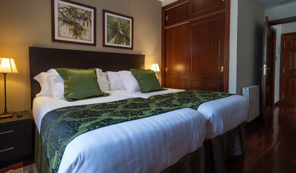 Habitación con dos camas individuales unidas con cabecera oscura y cojines verdes.