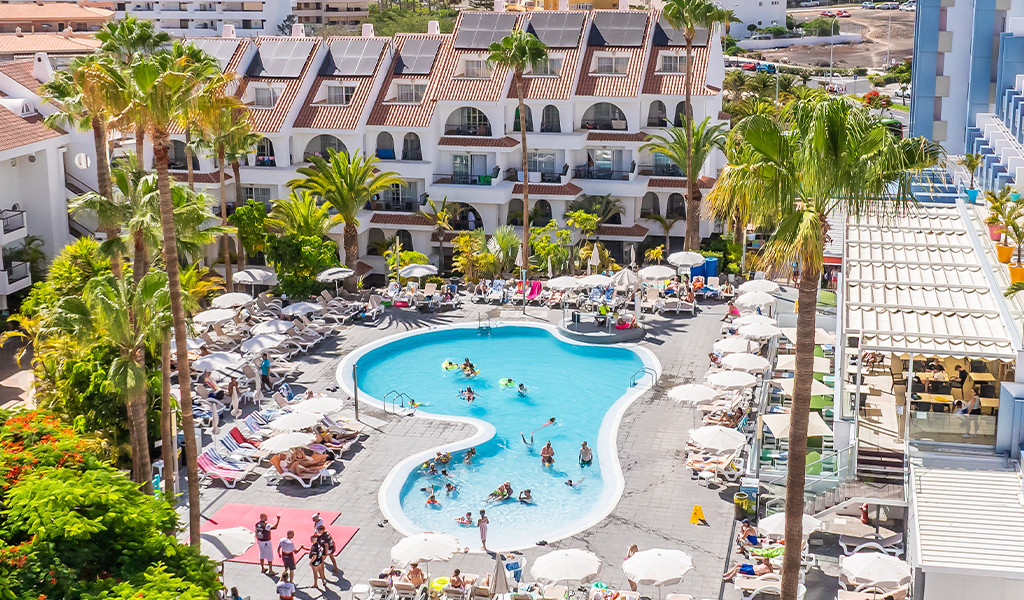 Personas disfrutando de la piscina del hotel en Tenerife rodeado de palmeras y sombrillas.