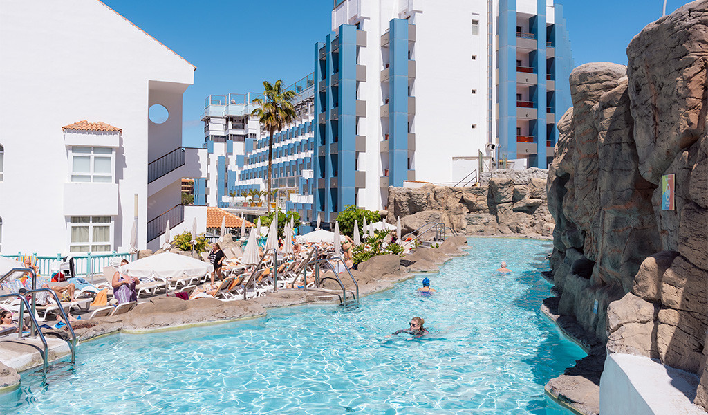 Piscina al aire libre rodeada de rocas y tumbonas en un hotel de Tenerife.