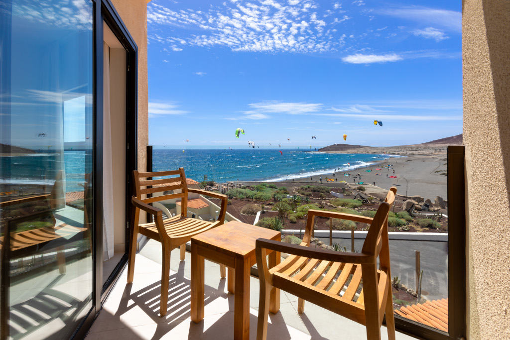 Vista desde terraza con sillas hacia la playa de El Médano, Tenerife, con personas practicando kitesurf.