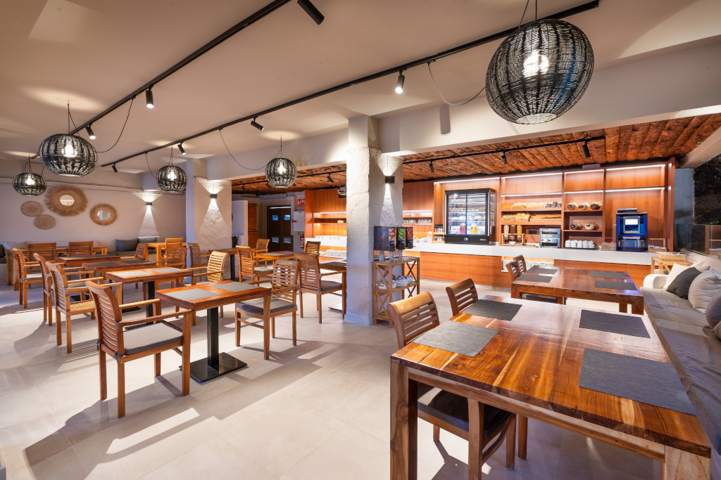 Cafetería en Tenerife con mesas de madera, sillas y mostrador iluminado.