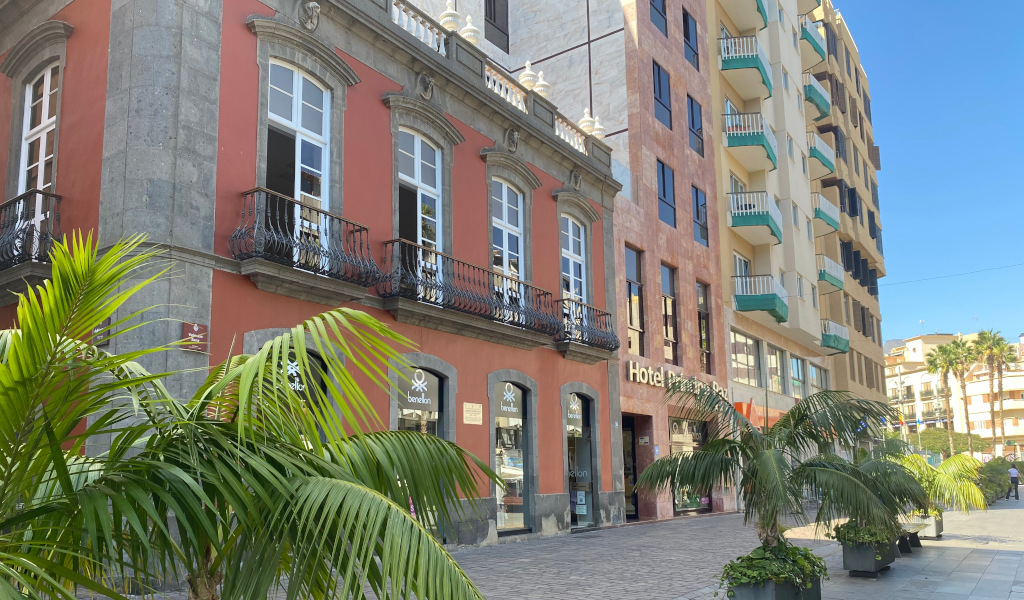 Edificio histórico junto al Hotel en Santa Cruz, Tenerife, con palmeras al frente.