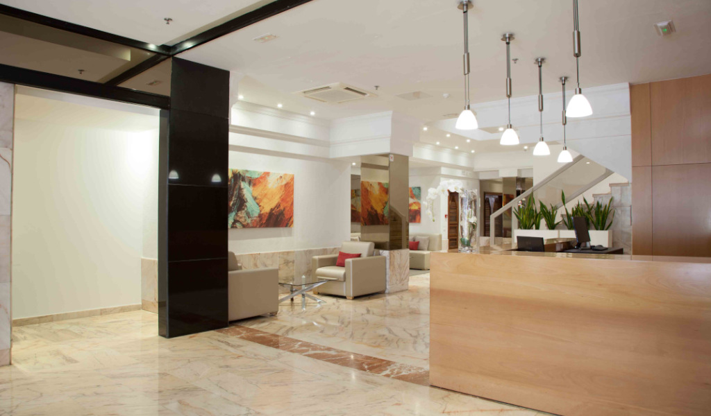 Vestíbulo moderno con sillas beige, plantas y luces colgantes en hotel de Tenerife.