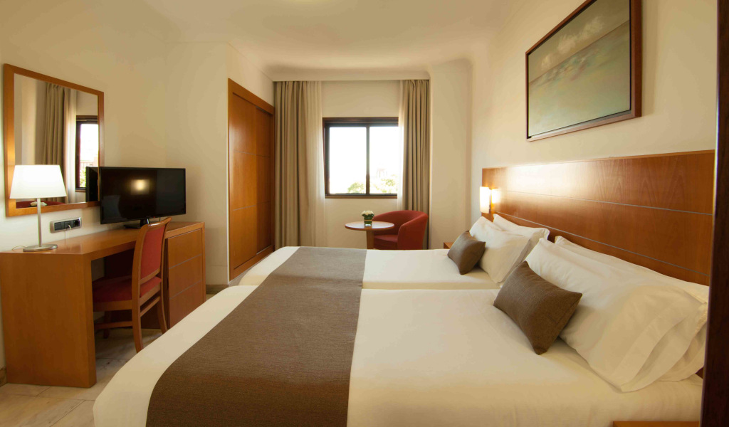 Habitación de hotel con dos camas, escritorio con televisor y ventana.
