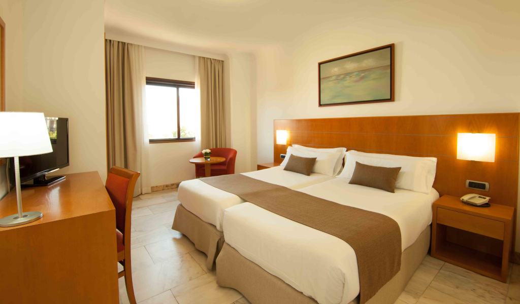 Habitación doble con camas individuales, escritorio, televisor y ventana en Tenerife.