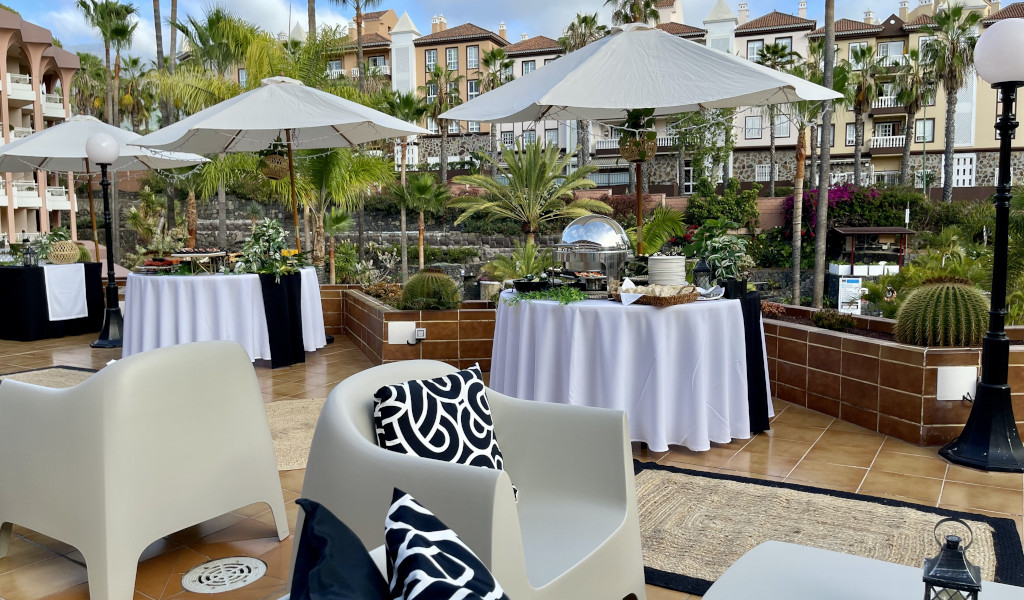 Terraza en Tenerife con mesas y sombrillas, rodeada de vegetación y edificaciones.