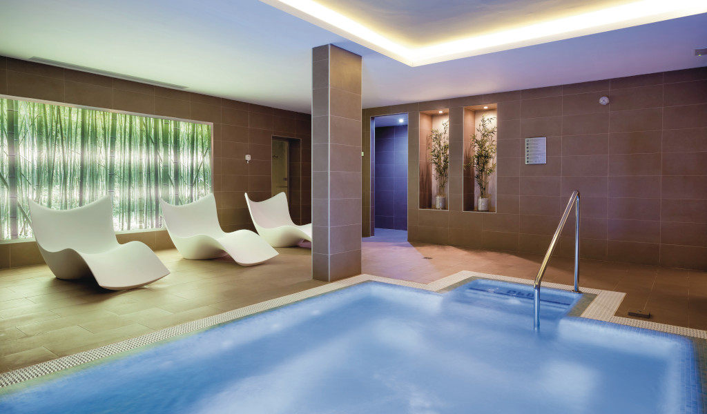 Piscina interior y área de descanso con sillas blancas en spa de Tenerife.