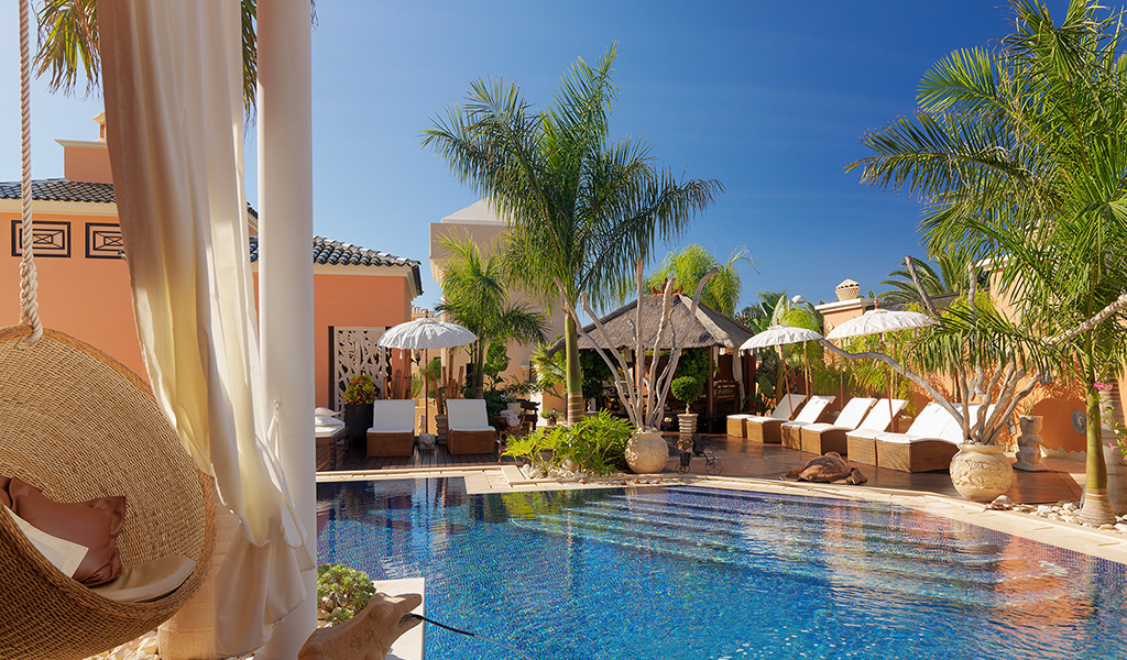 Piscina rodeada de tumbonas y palmeras en un hotel de Tenerife.