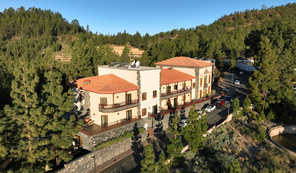 Edificio rodeado de pinos en Vilaflor, Tenerife, con coches estacionados enfrente.