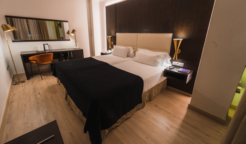 Cama doble en habitación de hotel en Santa Cruz de Tenerife con escritorio y espejo elegante.