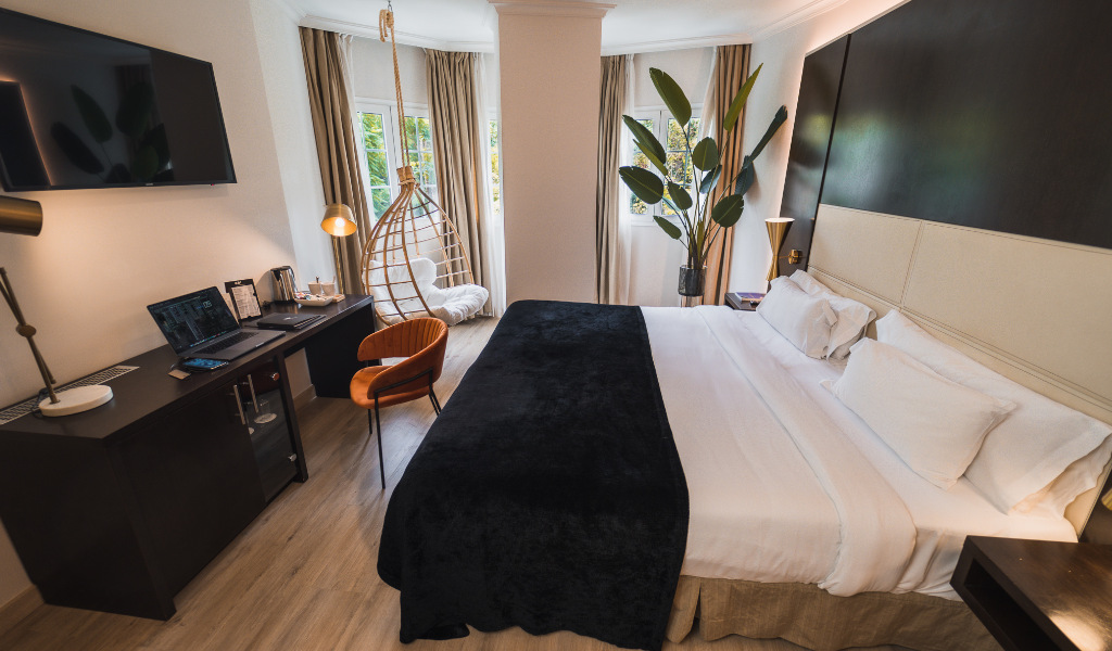 Habitación moderna con cama grande, escritorio con portátil y silla colgante en Tenerife.