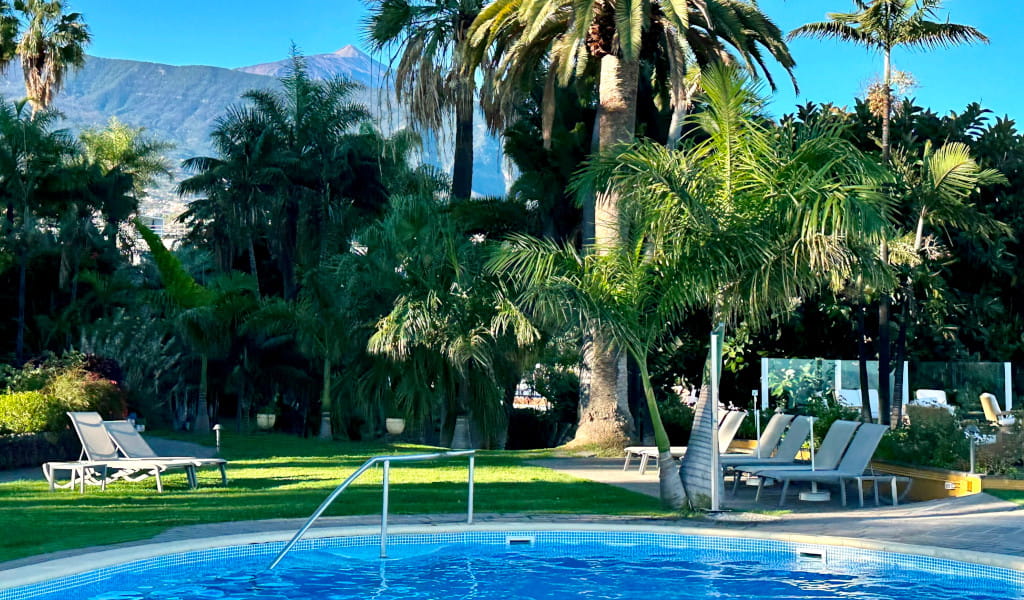 Piscina rodeada de palmeras en Puerto de la Cruz, Tenerife. Montañas al fondo.