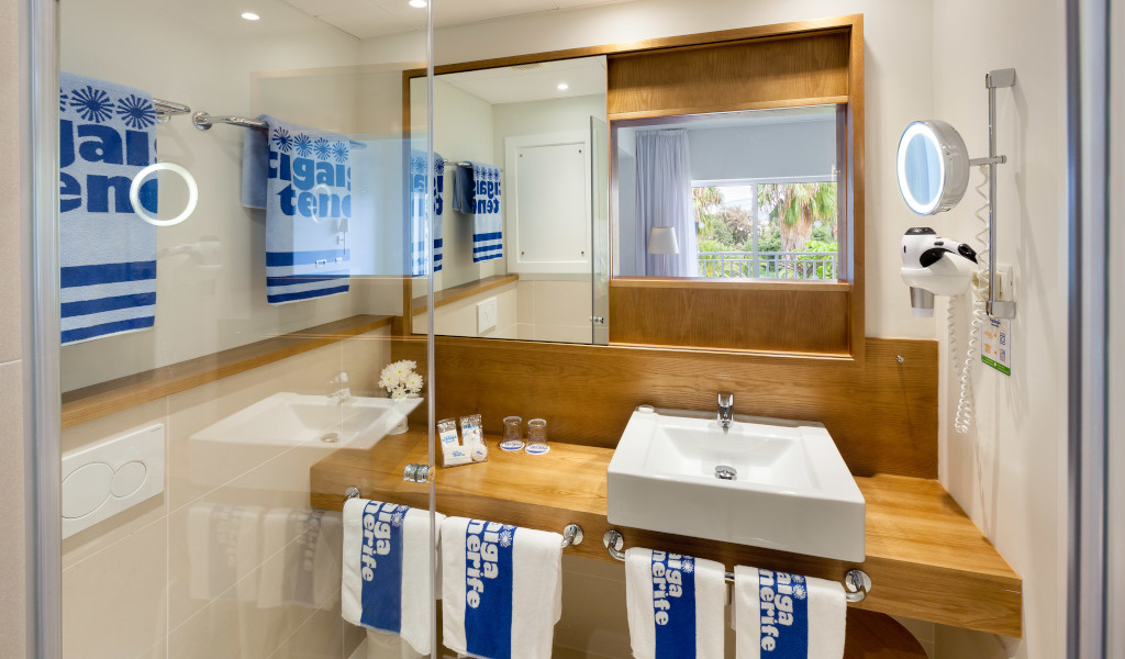 Baño moderno en un hotel de Tenerife con toallas azules y lavabo amplio.