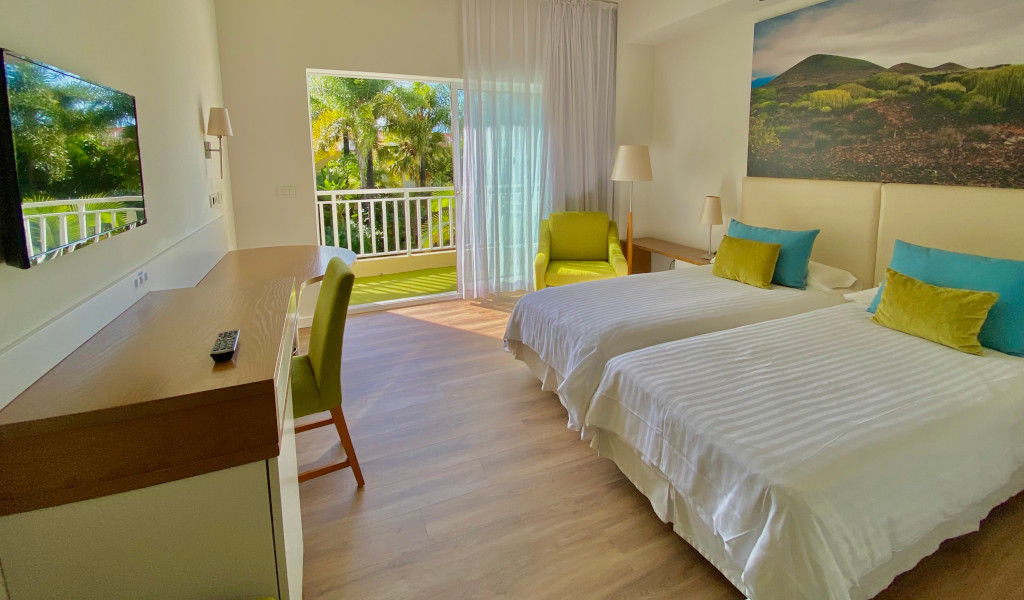 Habitación con dos camas, escritorio y balcón con vista a la vegetación en Tenerife.