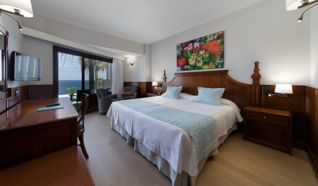 Habitación de hotel con vista al mar en Tenerife, cama doble y decoración floral.