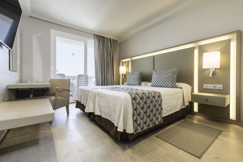 Cama matrimonial en habitación de hotel moderno en Tenerife con vista al exterior.