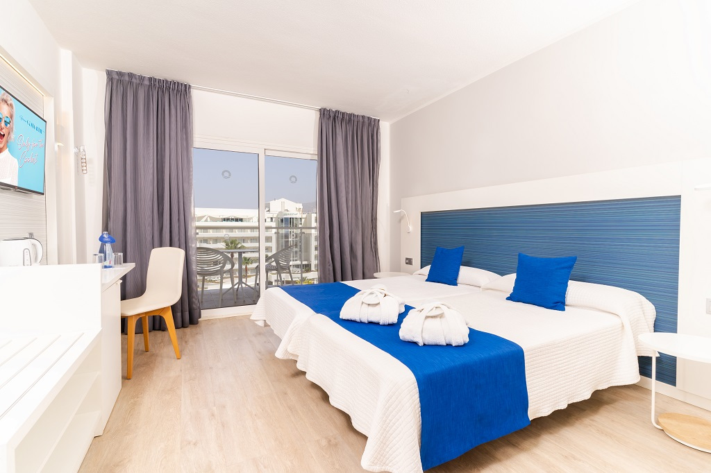 Habitación doble con balcón en hotel de Tenerife, camas con albornoces sobre ellas.
