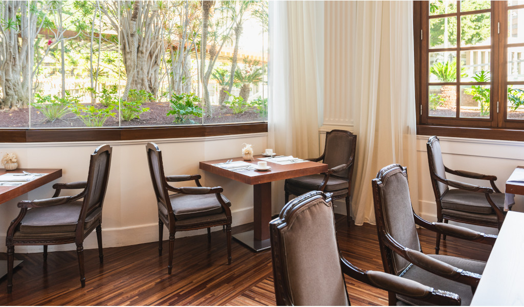 Comedor de restaurante en Tenerife con sillas, mesas y ventanas grandes.