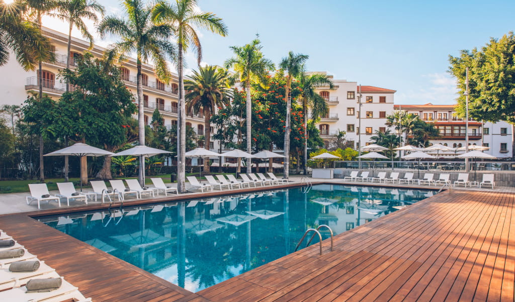 Piscina al aire libre con palmeras y tumbonas en hotel de Tenerife.